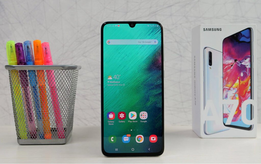 هاتف Samsung Galaxy A70 وعلبته ومجموعة أقلام ملونة بجانبه
